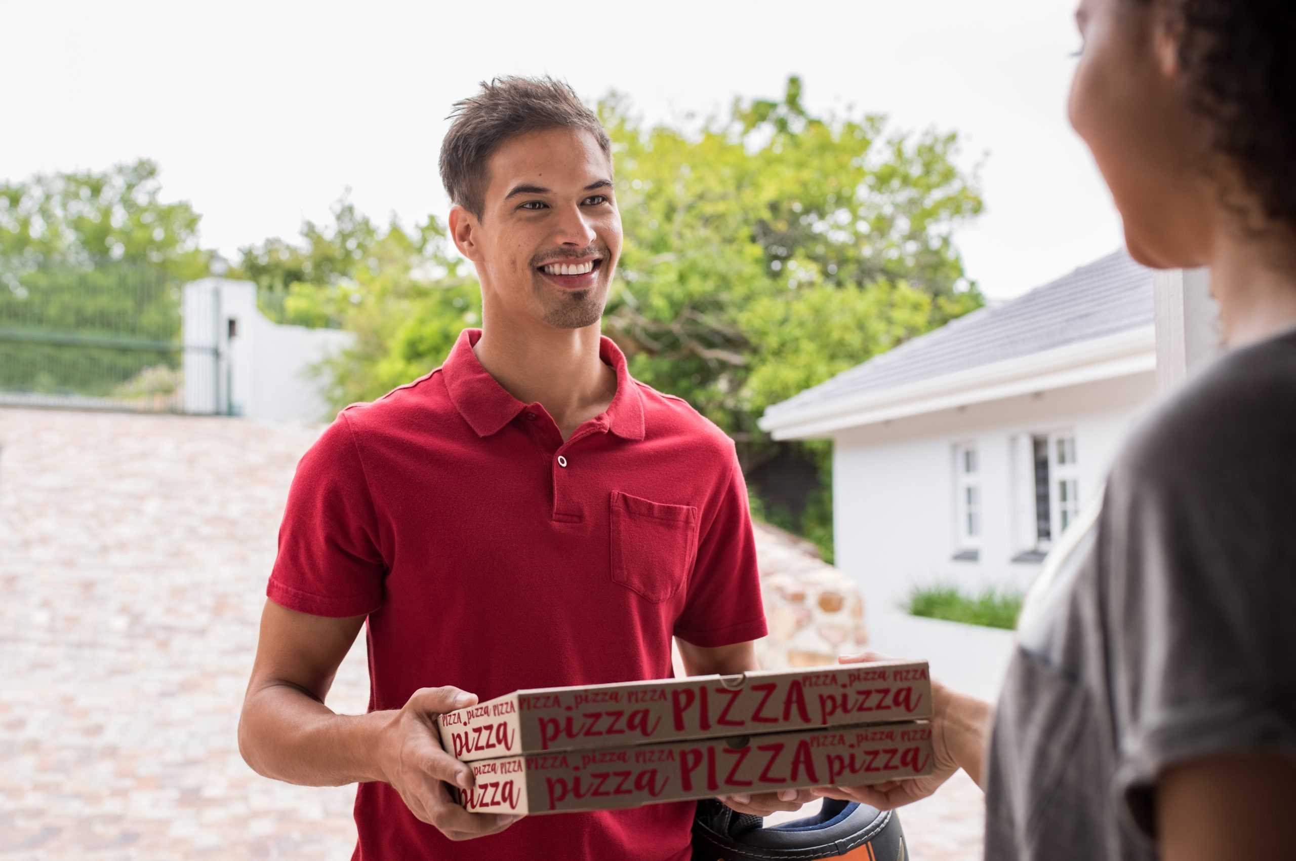 Smiling delivery boy in red t-shirt delivering two pizza boxes to woman. Happy young delivery man giving pizza to customer on the doorstep. Smiling woman receiving take away food from deliveryman.